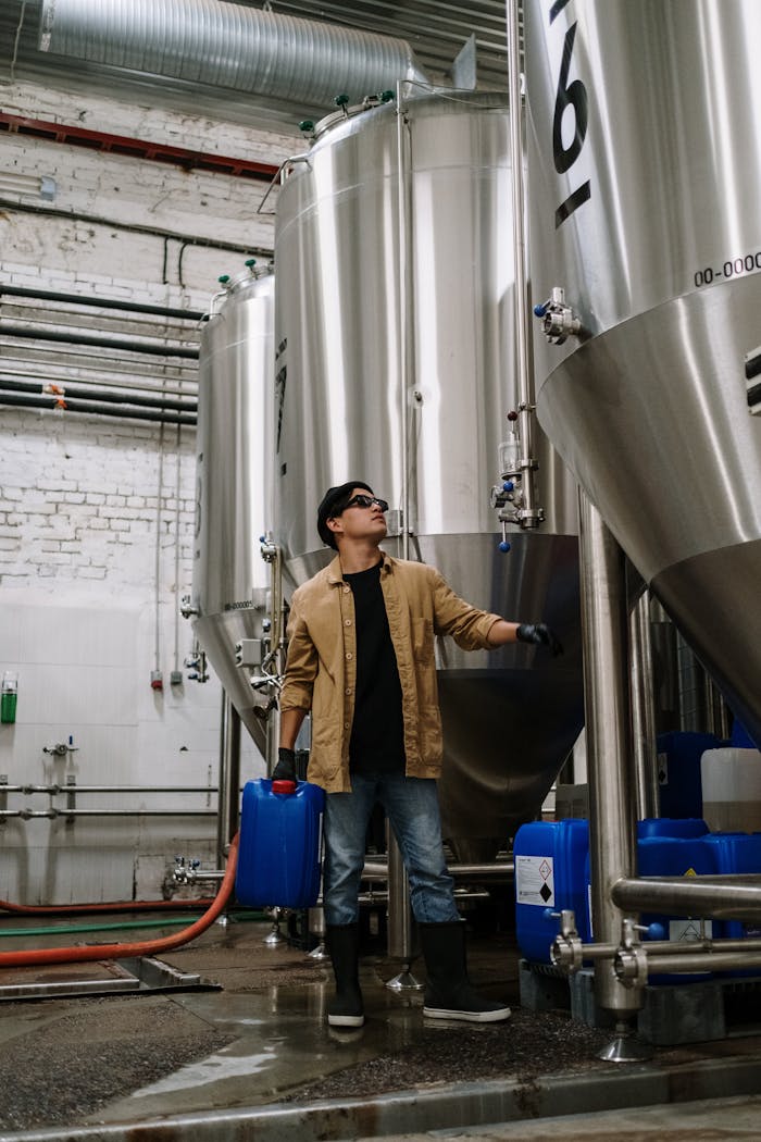 Man in industrial setting checking stainless steel brewing equipment.